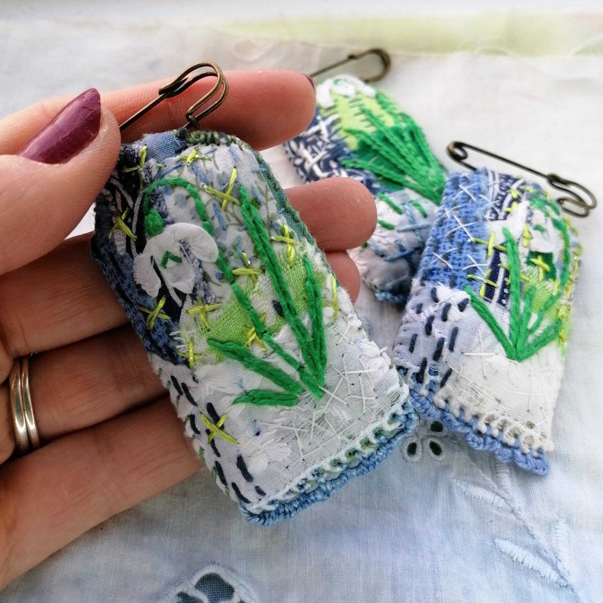Tag shaped, padded and embroidered snowdrop brooches on vintage style bronze tone kilt pins. Style 1 pictured in Paula's hand for scale.