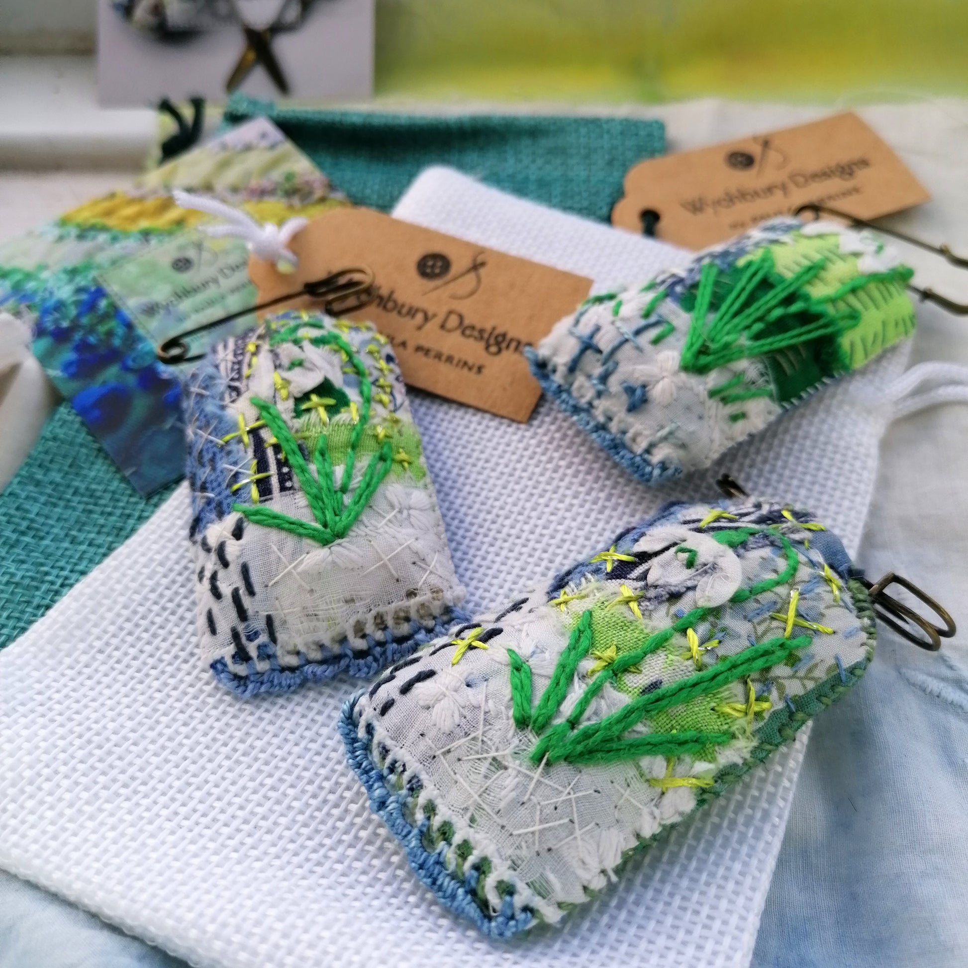 Tag shaped, padded and embroidered snowdrop brooches on vintage style bronze tone kilt pins pictured with gift bags