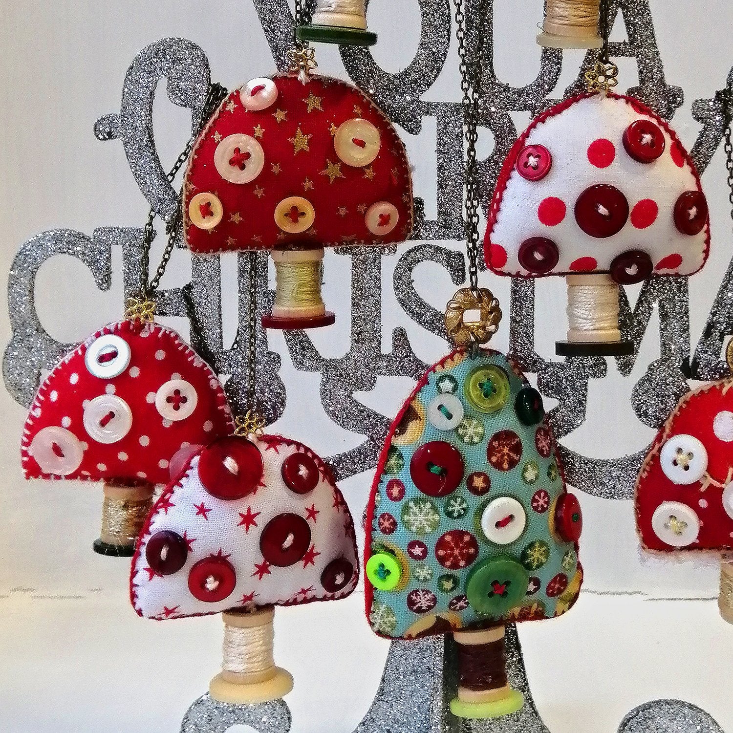 Collection of fabric toadstool ornaments with buttons and spools hanging from a silver glitter tree.